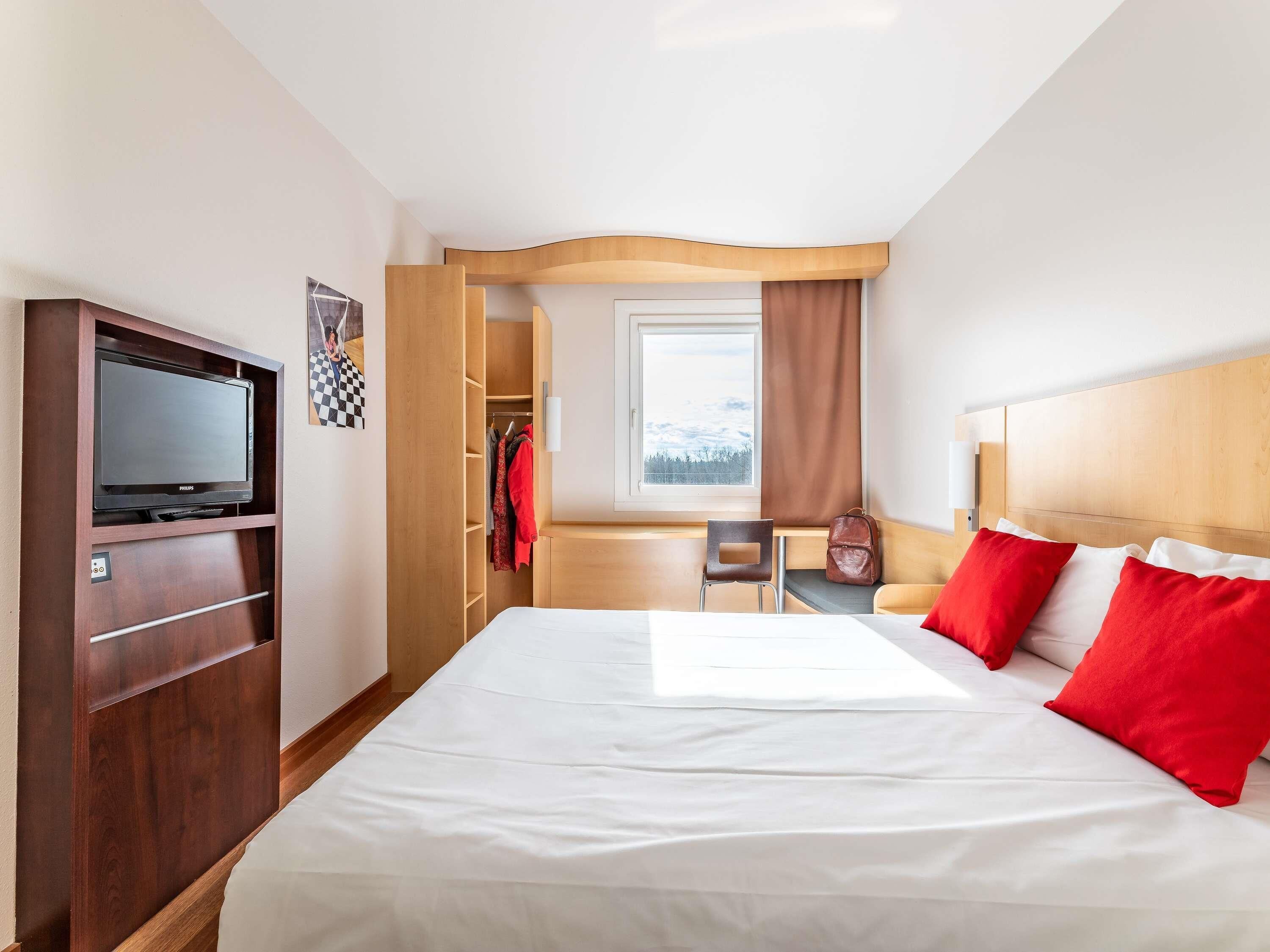 Una habitación de hotel con cama, televisor, escritorio y ventana.