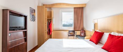 Una habitación de hotel con cama, televisor, escritorio y ventana.