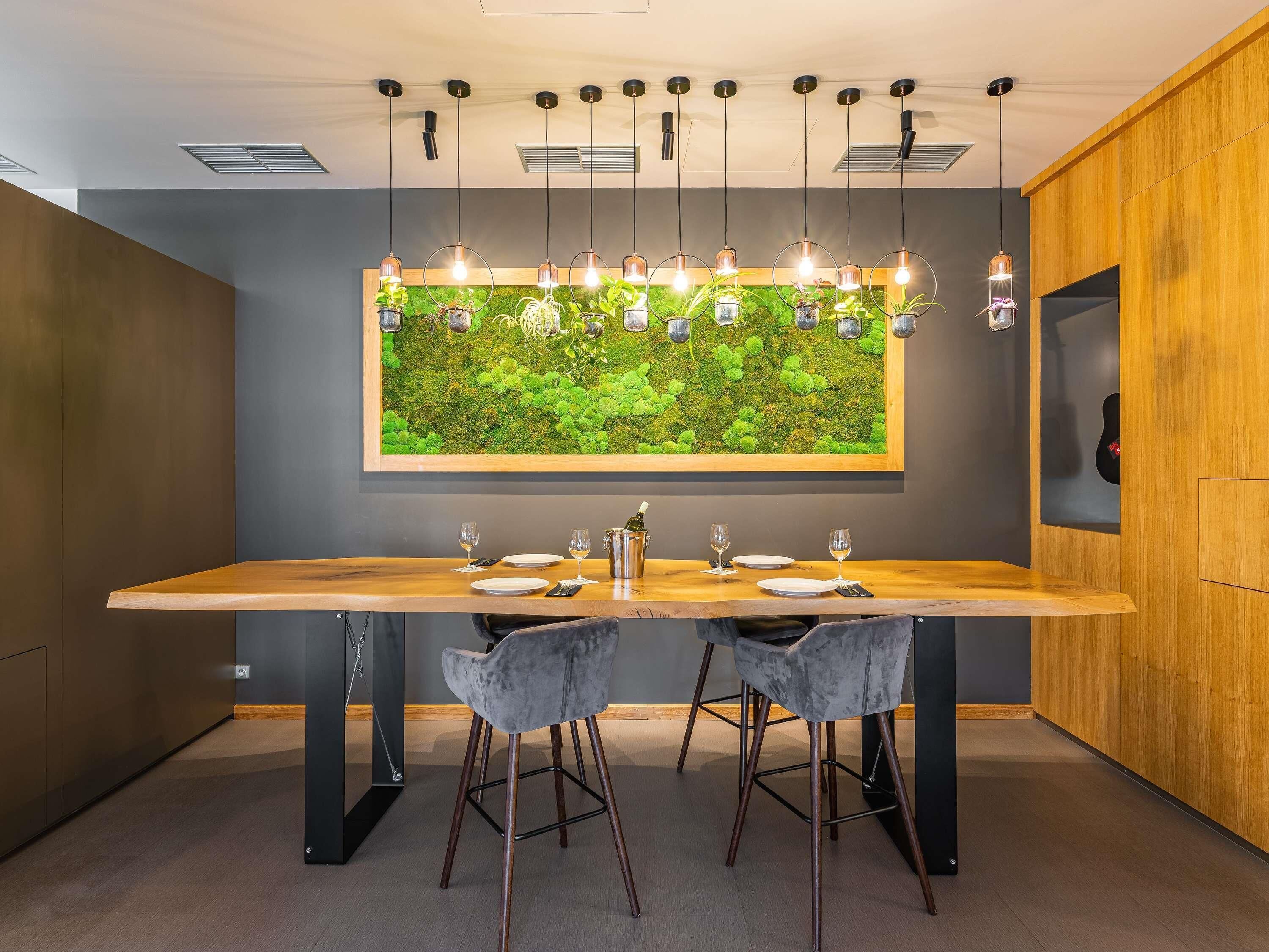 Un espace repas moderne avec une longue table, deux chaises grises et un luminaire suspendu.