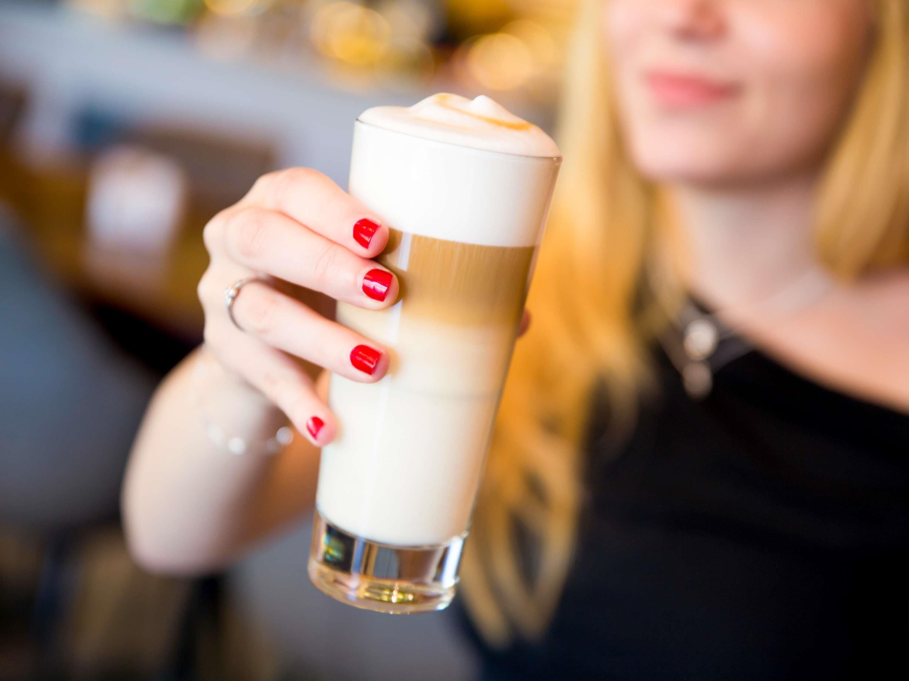 A person holding a tall glass with a layered beverage.