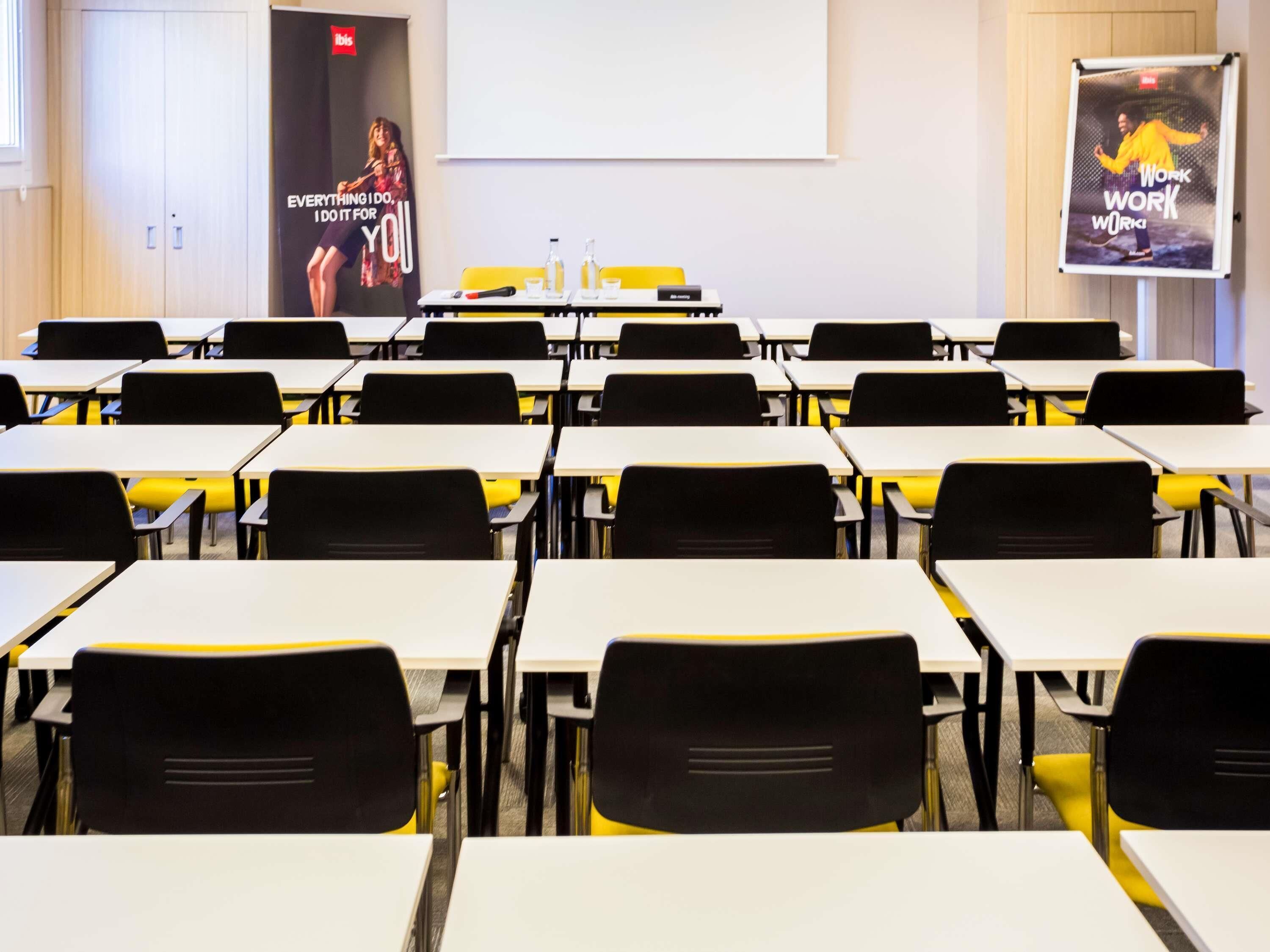A classroom with rows of desks and chairs, a projector screen, and two posters on the walls.