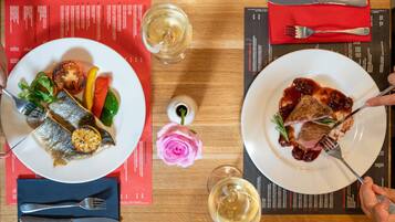 Two plates of food, a fork, a knife, and a glass of white wine on a wooden table.