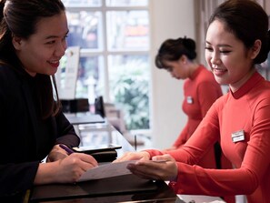 A person in a red uniform sitting at a table with a name tag, another person in a black outfit, and a third person in the background.