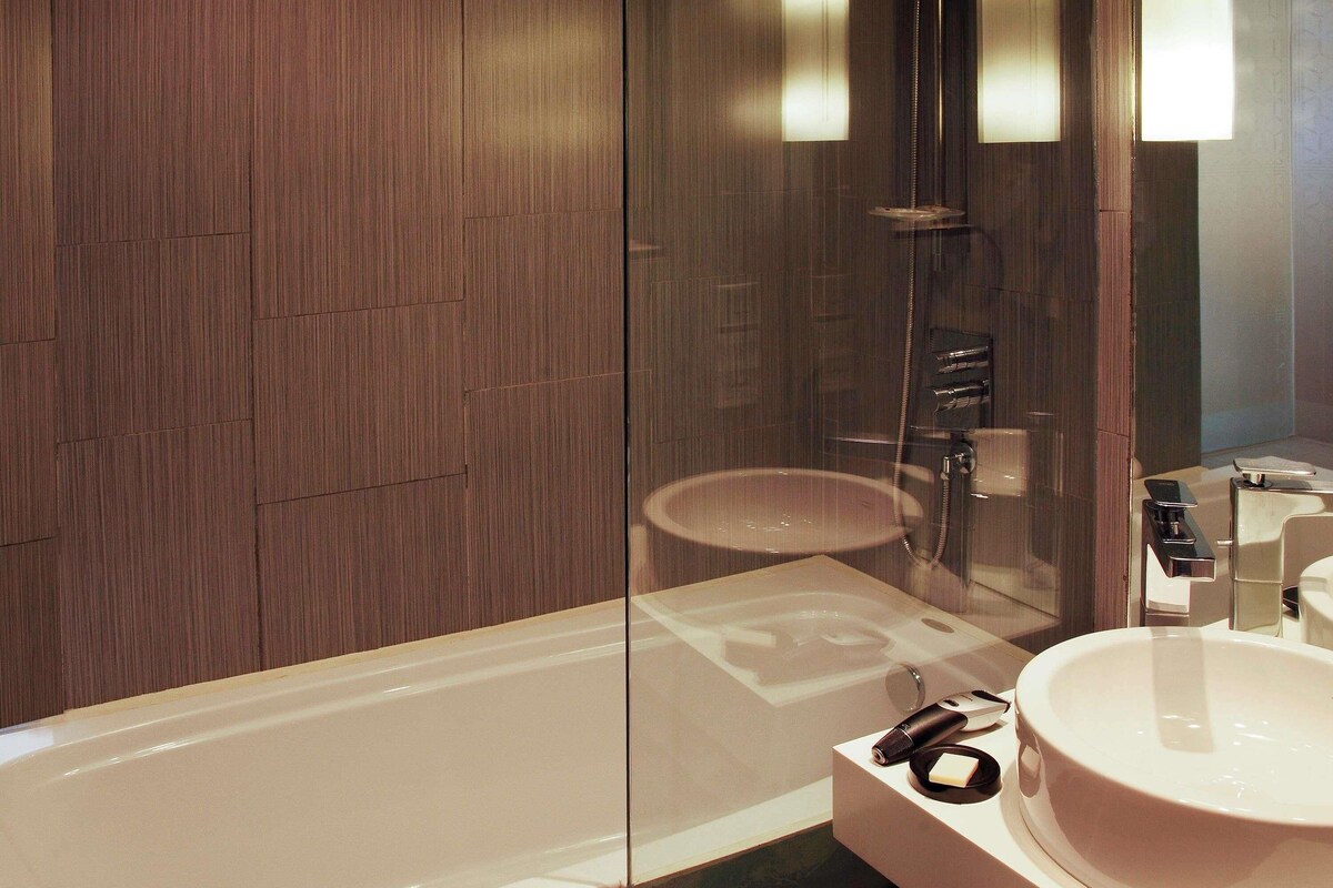 A modern bathroom with a bathtub, a glass-enclosed shower, and a vanity with a sink and mirror.