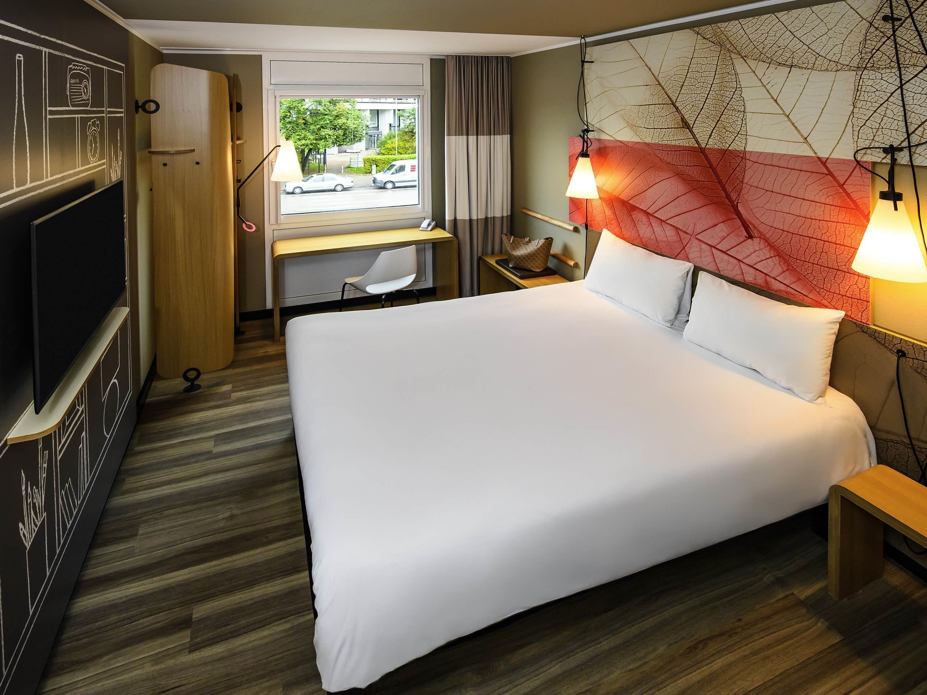 A hotel room with a bed, a desk, a TV, and a view of the street.