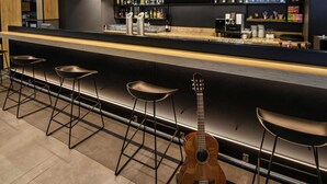 A bar area with a long counter, multiple stools, and a guitar. - ibis Muenchen City West (Munich)
