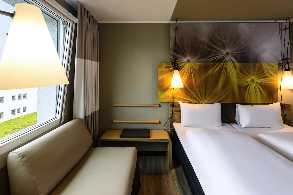 A hotel room with a bed, a sofa, a nightstand, and a lamp.