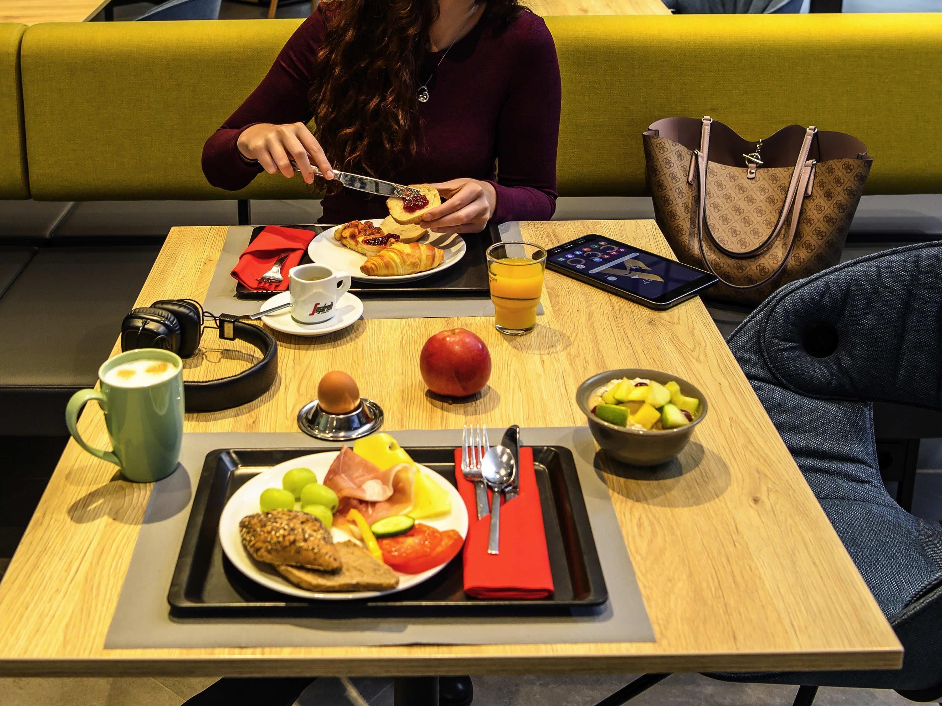A breakfast setting with a variety of food items, a beverage, and a handbag on a table.