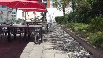 An outdoor dining area with tables and chairs, red umbrellas, and a gravel path.