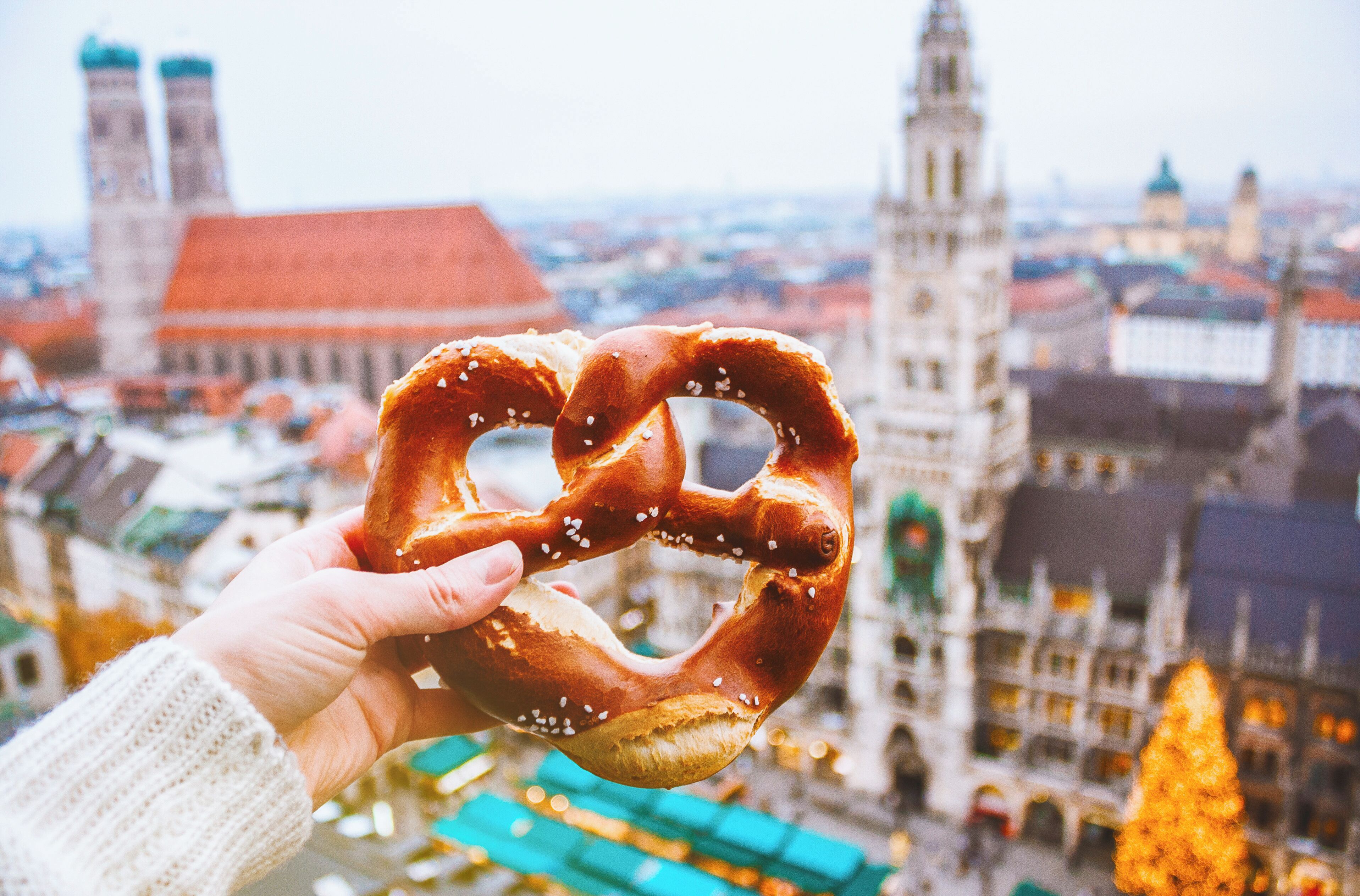 A hand holding a pretzel with a cityscape in the background.