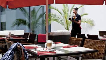 An outdoor dining area with wicker furniture, red umbrellas, and a waiter serving.