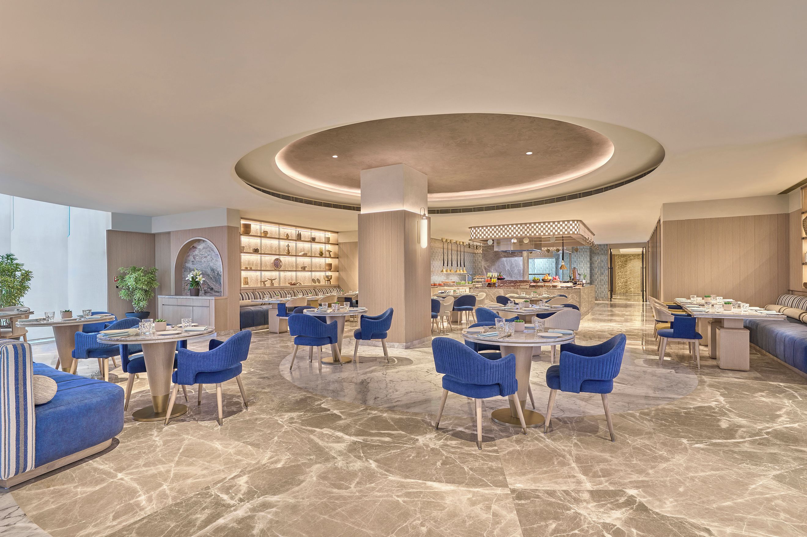 A spacious hotel lobby with multiple seating areas, a central column, and a view into the dining area.
