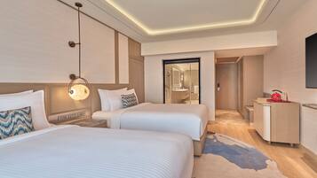 Habitación de hotel con dos camas, un escritorio, un espejo y un baño visible a través de una puerta abierta.