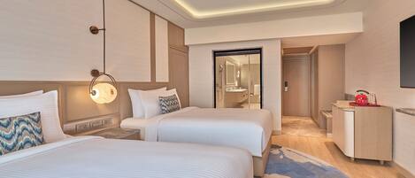 A hotel room with two beds, a desk, a mirror, and a bathroom visible through an open door.