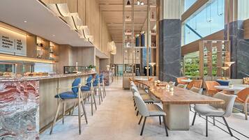 Interior moderno de una cafetería con una barra larga, zona de estar y amplias ventanas.