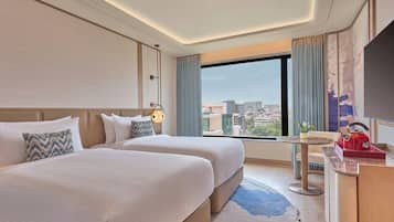 A hotel room with two beds, a desk, a chair, a TV, and a city view.