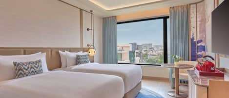 A hotel room with two beds, a desk, a chair, a TV, and a city view.