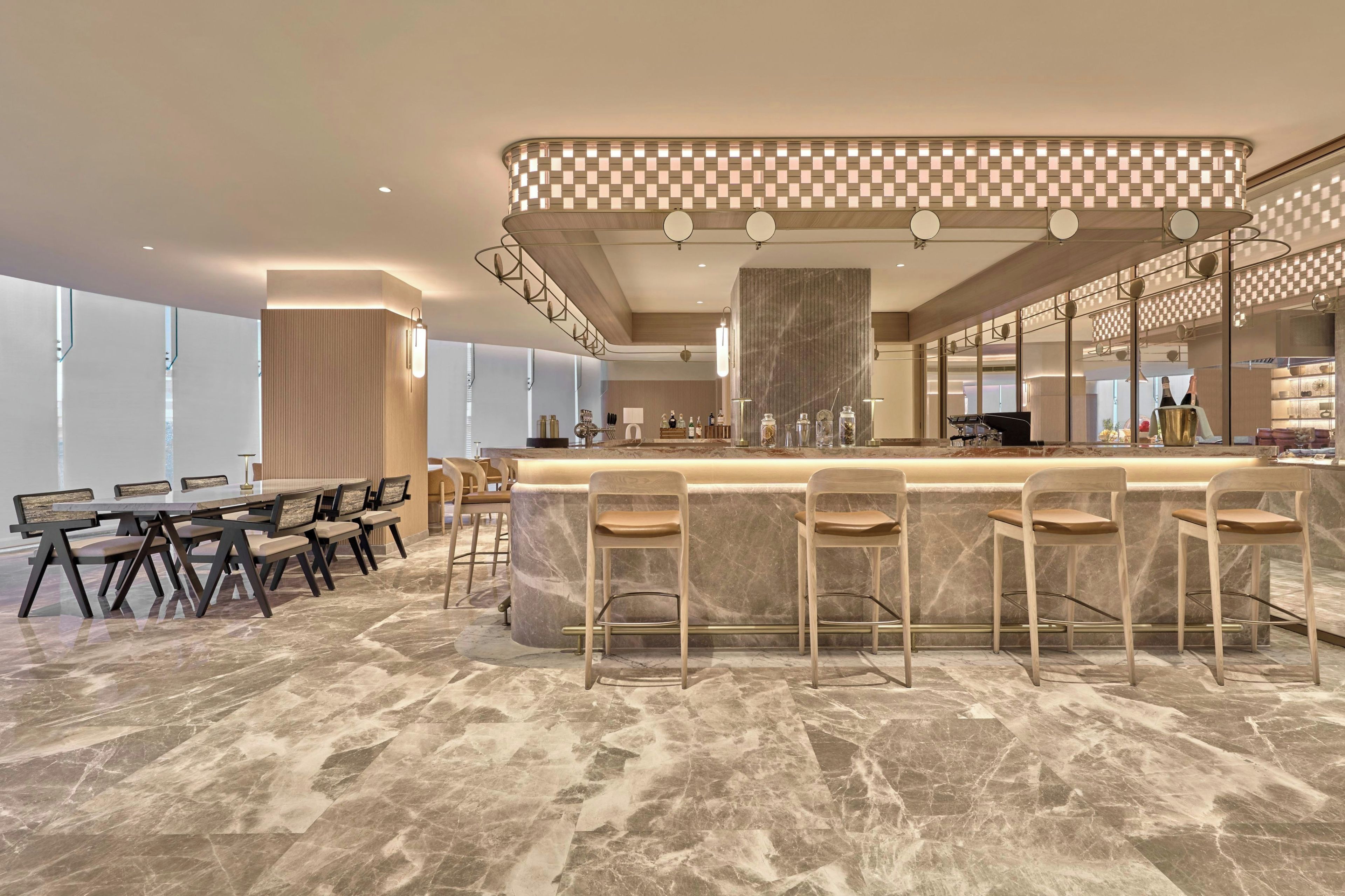 A modern bar area with a marble countertop, bar stools, and a high ceiling with recessed lighting.