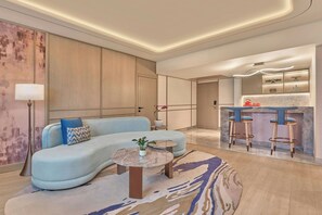 A modern living room with a curved sofa, a round coffee table, and a kitchen area with bar stools. - Athiva Pulse Navi Mumbai, Autograph Collection (Navi Mumbai)