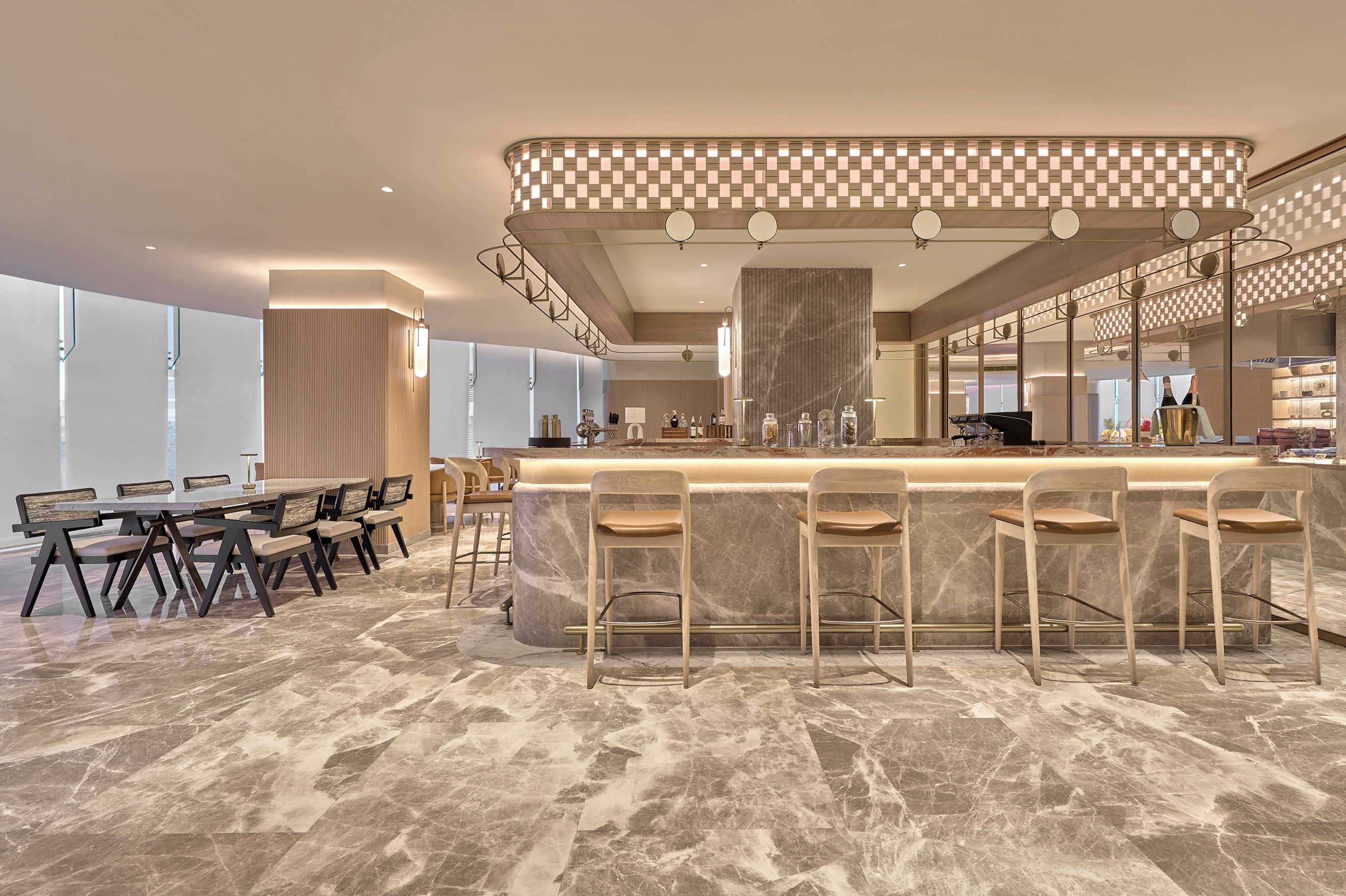 Un área de bar moderna con mostrador de mármol, taburetes y un techo alto con iluminación empotrada.