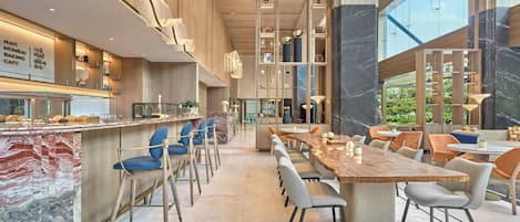 A modern cafe interior with marble countertops, seating, and a large window offering a view of greenery.