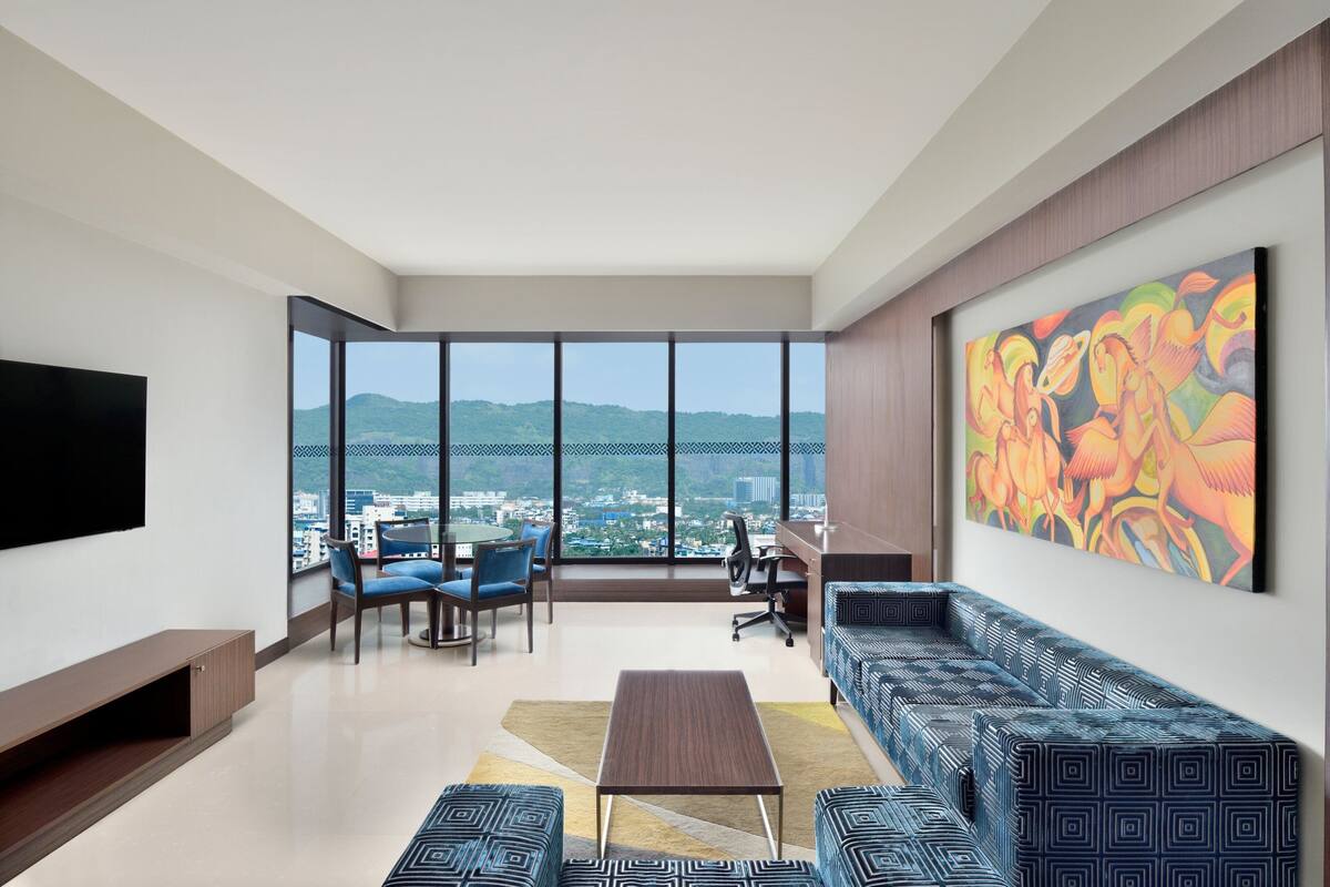 A modern living room with a large window, a sofa, a coffee table, and a painting on the wall.