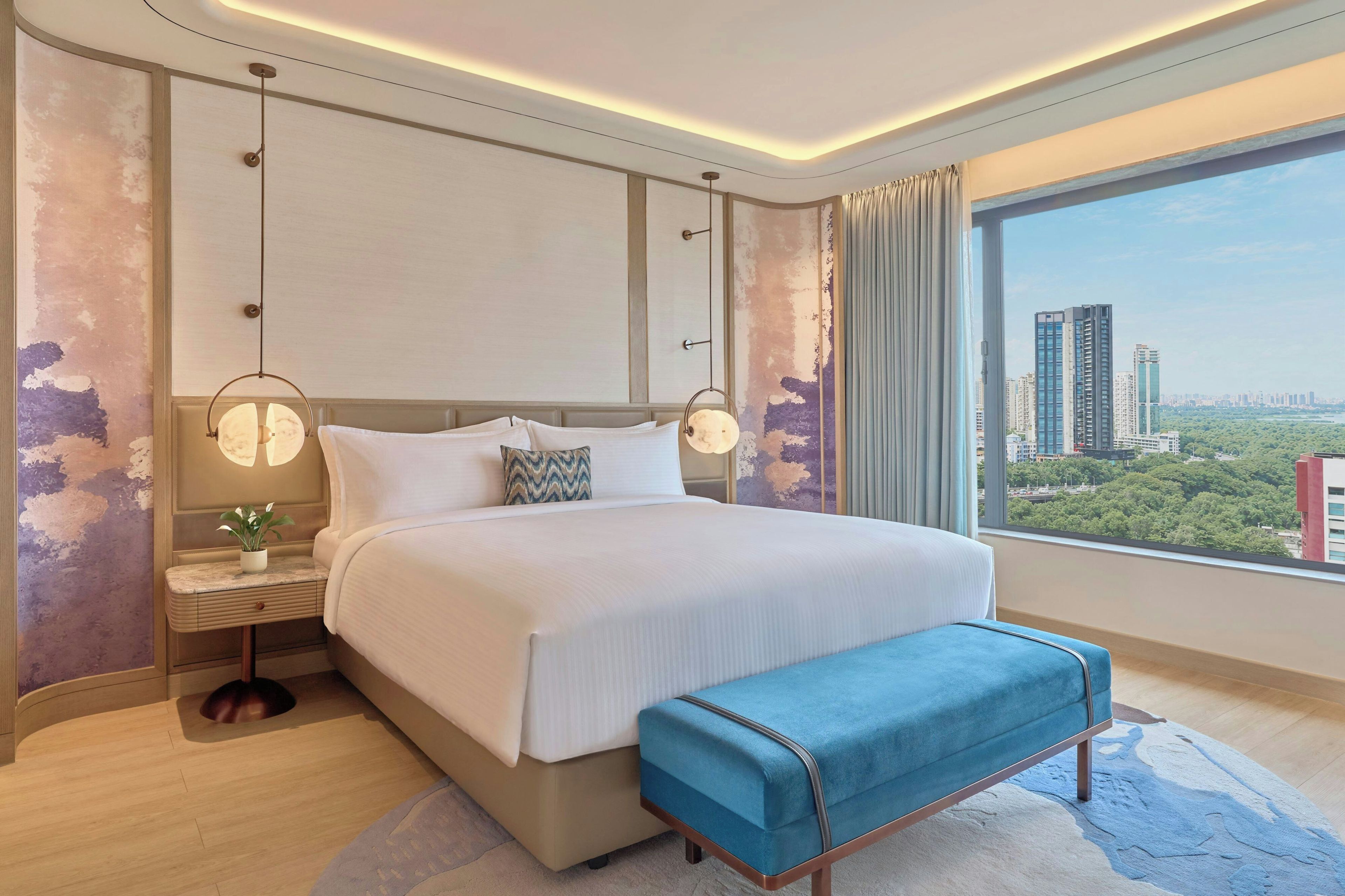A modern hotel room with a large bed, bedside tables, a view of the city, and a cityscape through the window.