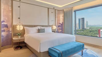 A modern hotel room with a large bed, bedside tables, a view of the city, and a cityscape through the window.