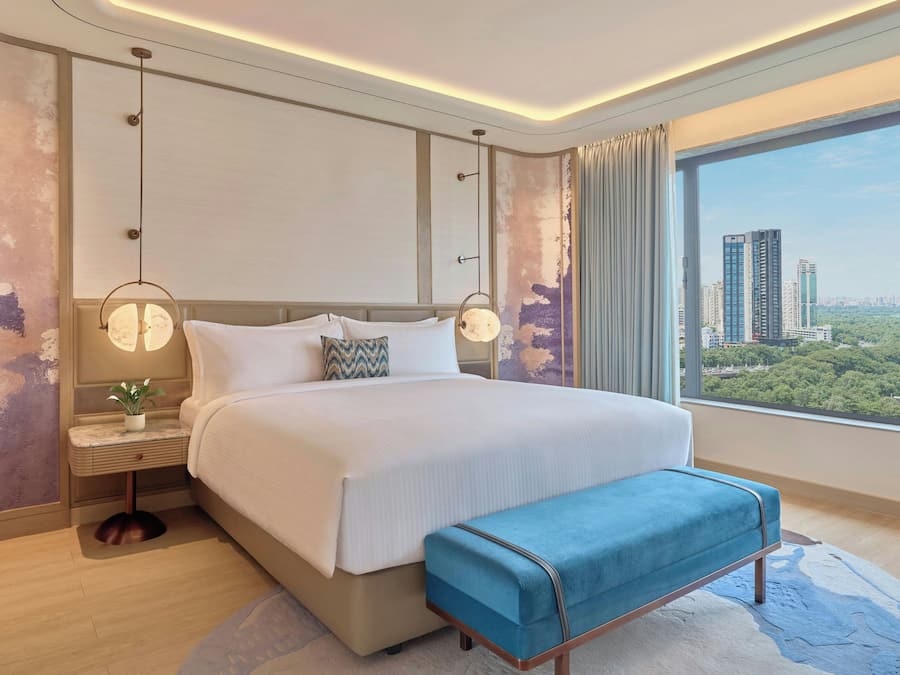 Una habitación de hotel moderna con una cama grande, mesitas de noche y vistas de la ciudad a través de la ventana.