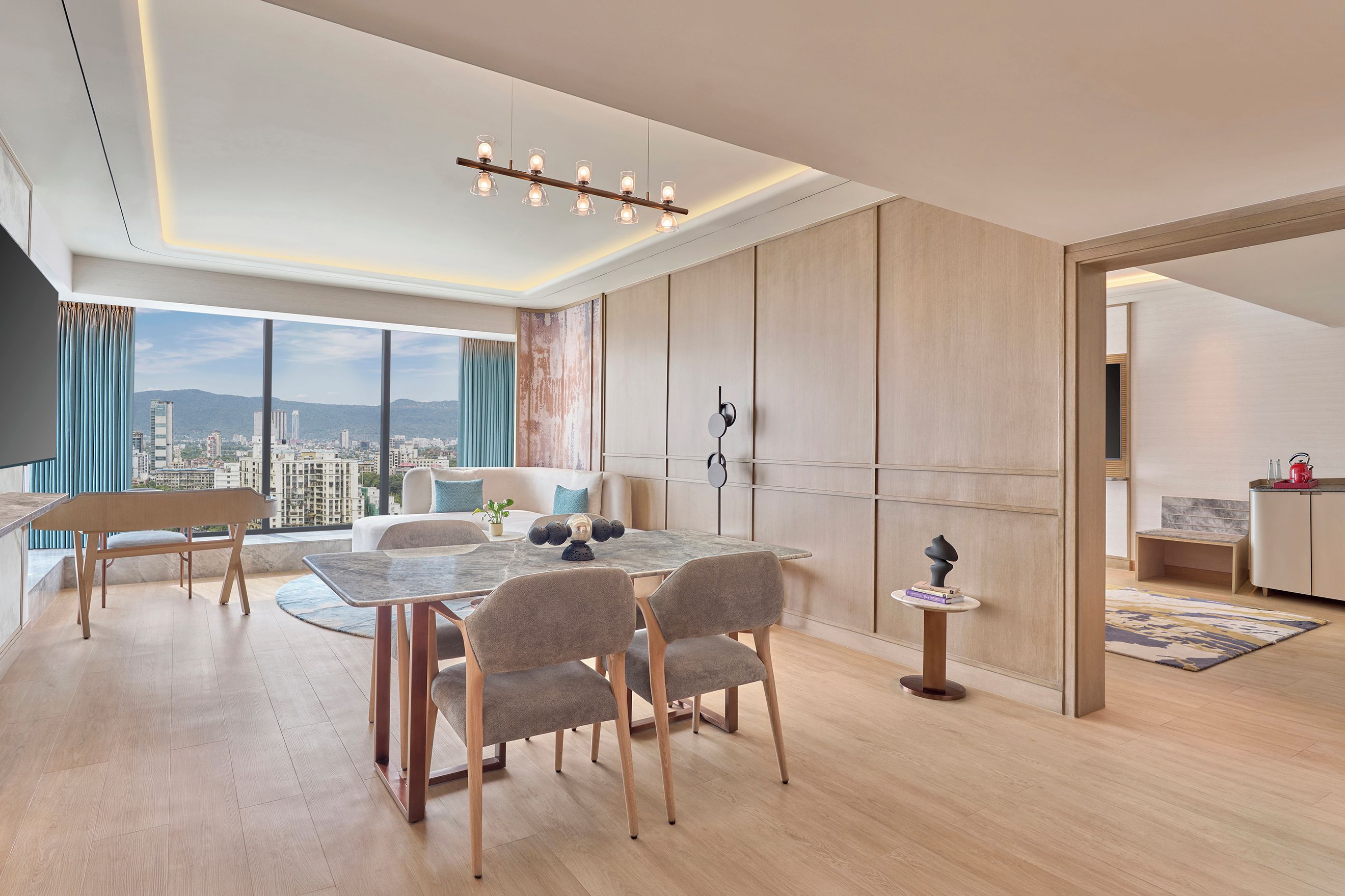 A modern living room with a dining area, large windows, and a view of the cityscape.