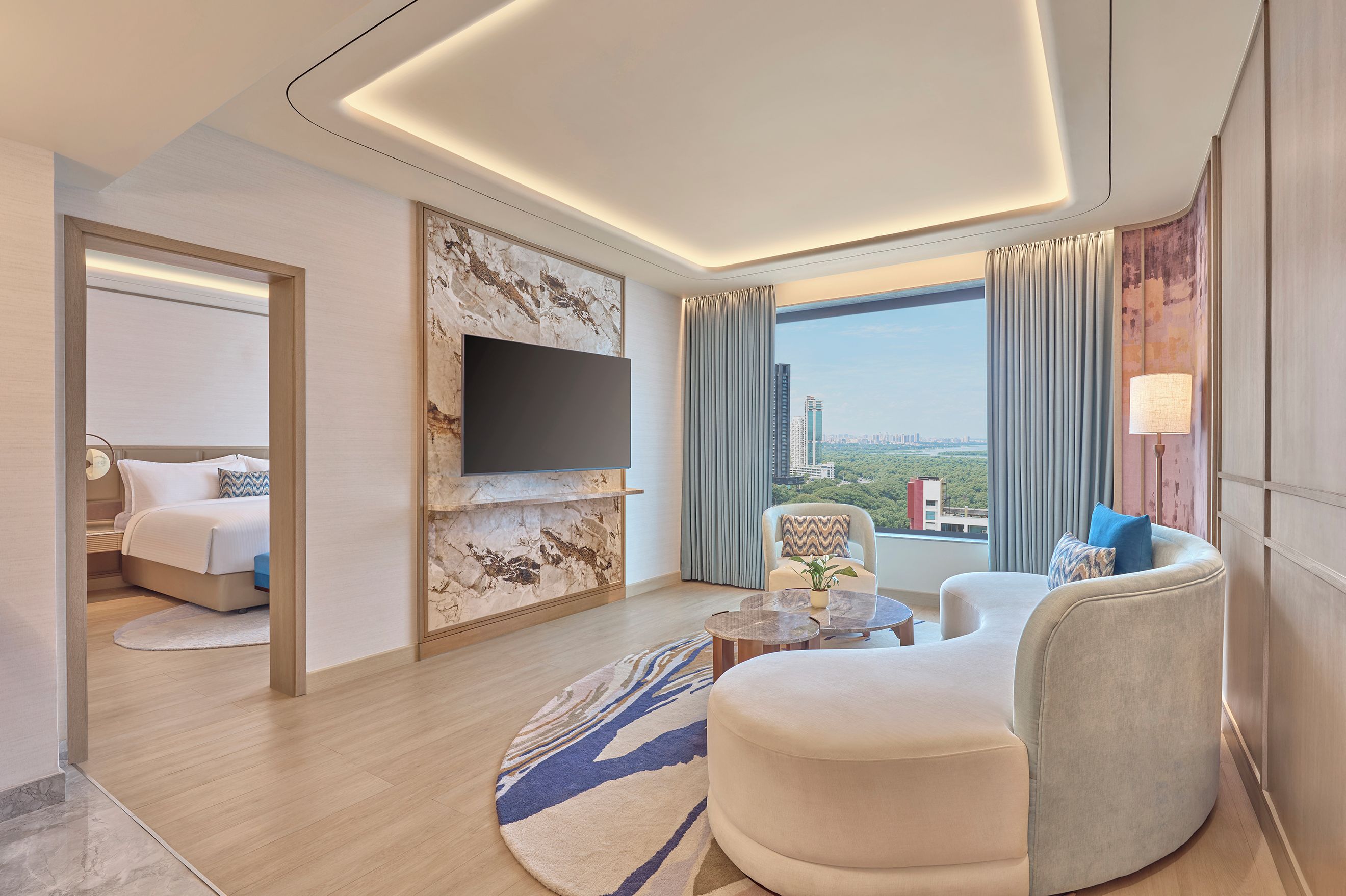 A modern hotel room with a bed, seating area, flat-screen TV, and a city view.