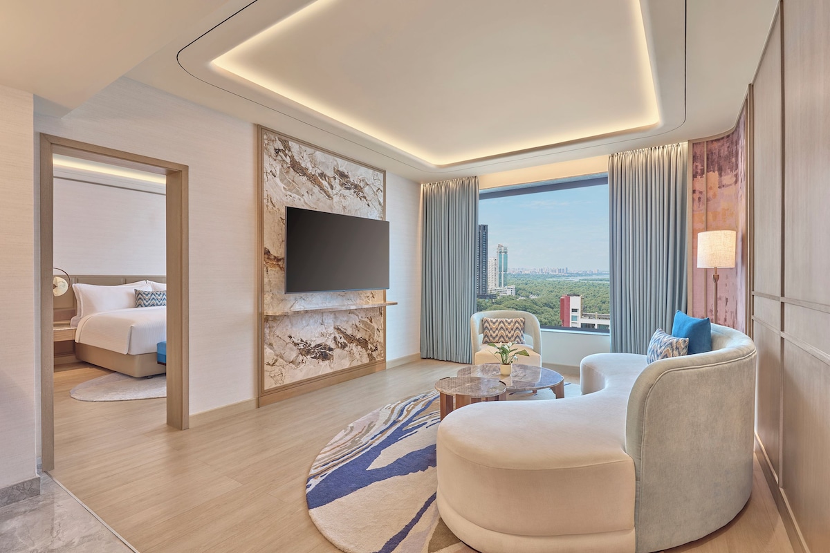 Habitación de hotel moderna con cama, zona de estar, televisor y vistas a la ciudad.
