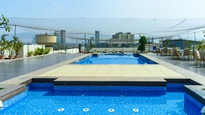 Piscina en la azotea con vistas a la ciudad, rodeada de plantas en macetas y mobiliario de exterior.