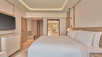 A hotel room with a large bed, a flat-screen TV, a wooden wardrobe, and a bathroom visible through an open door.