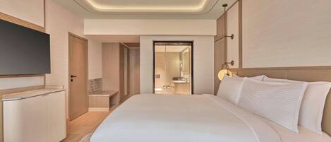Quarto de hotel com uma cama grande, televisão de tela plana, guarda-roupa de madeira e banheiro visível através de uma porta aberta.