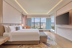 Una habitación de hotel moderna con una cama grande, zona de estar, televisor y vista a la ciudad.