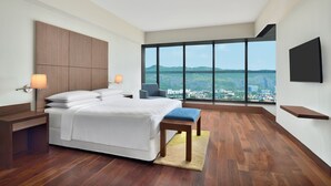 Ein modernes Hotelzimmer mit einem großen Bett, einem Schreibtisch, einem Sessel und einem an der Wand befestigten Fernseher.