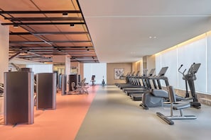 Un gimnasio con equipo de ejercicio, incluyendo cintas de correr y máquinas de pesas, y un largo pasillo con alfombra roja.