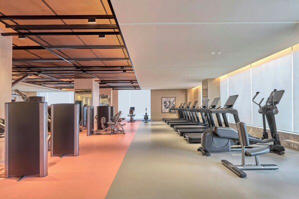 Un gimnasio con equipo de ejercicio, incluyendo cintas de correr y máquinas de pesas, y un largo pasillo.
