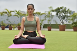 A person sitting on a pink yoga mat outdoors with potted plants in the background. - Athiva Pulse Navi Mumbai, Autograph Collection (Navi Mumbai)