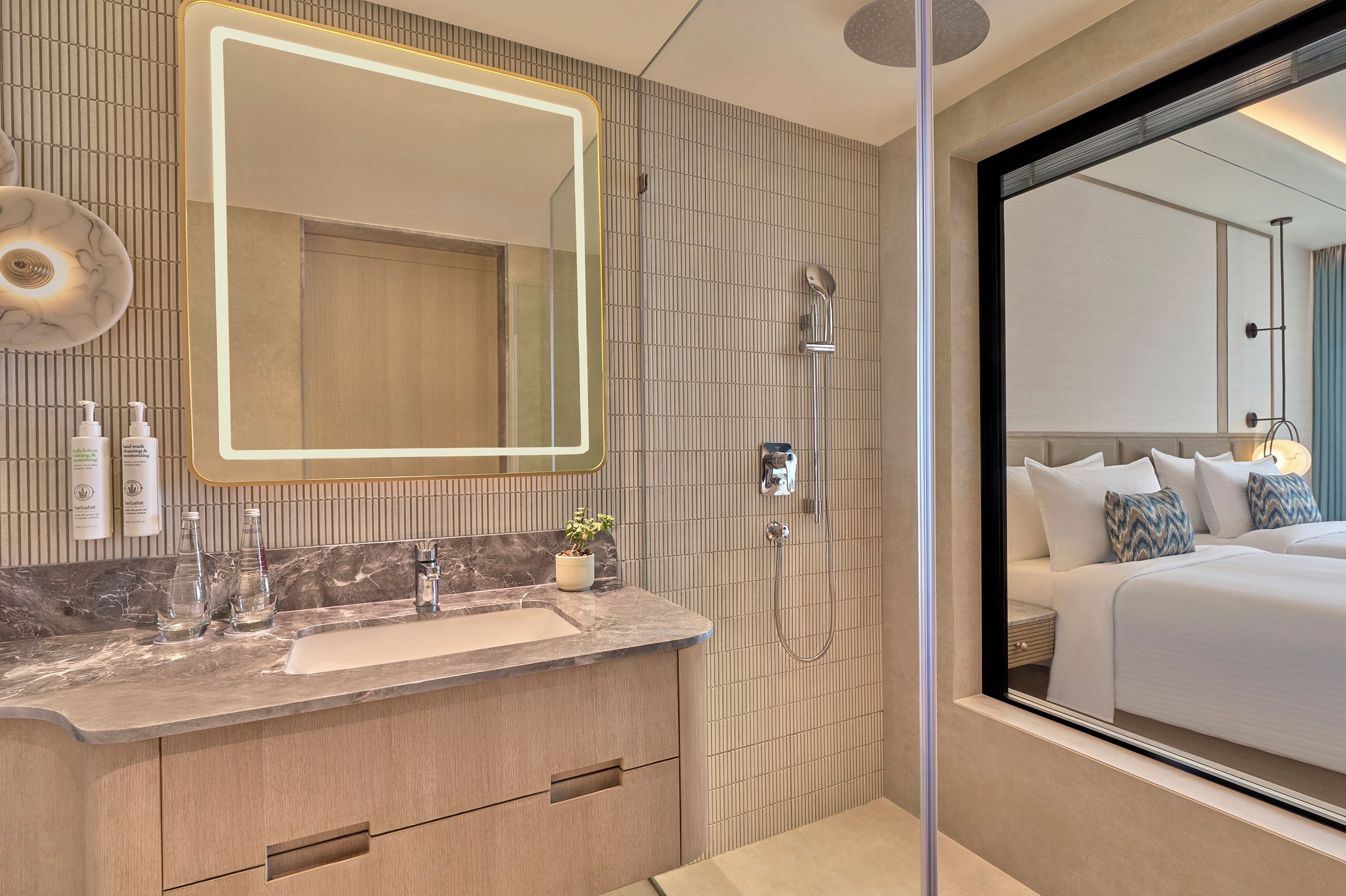 Un baño moderno con tocador, un espejo grande, ducha y vista a un dormitorio.