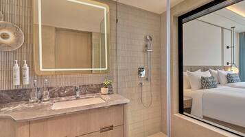 Un baño moderno con tocador, un espejo grande, ducha y vista a un dormitorio.