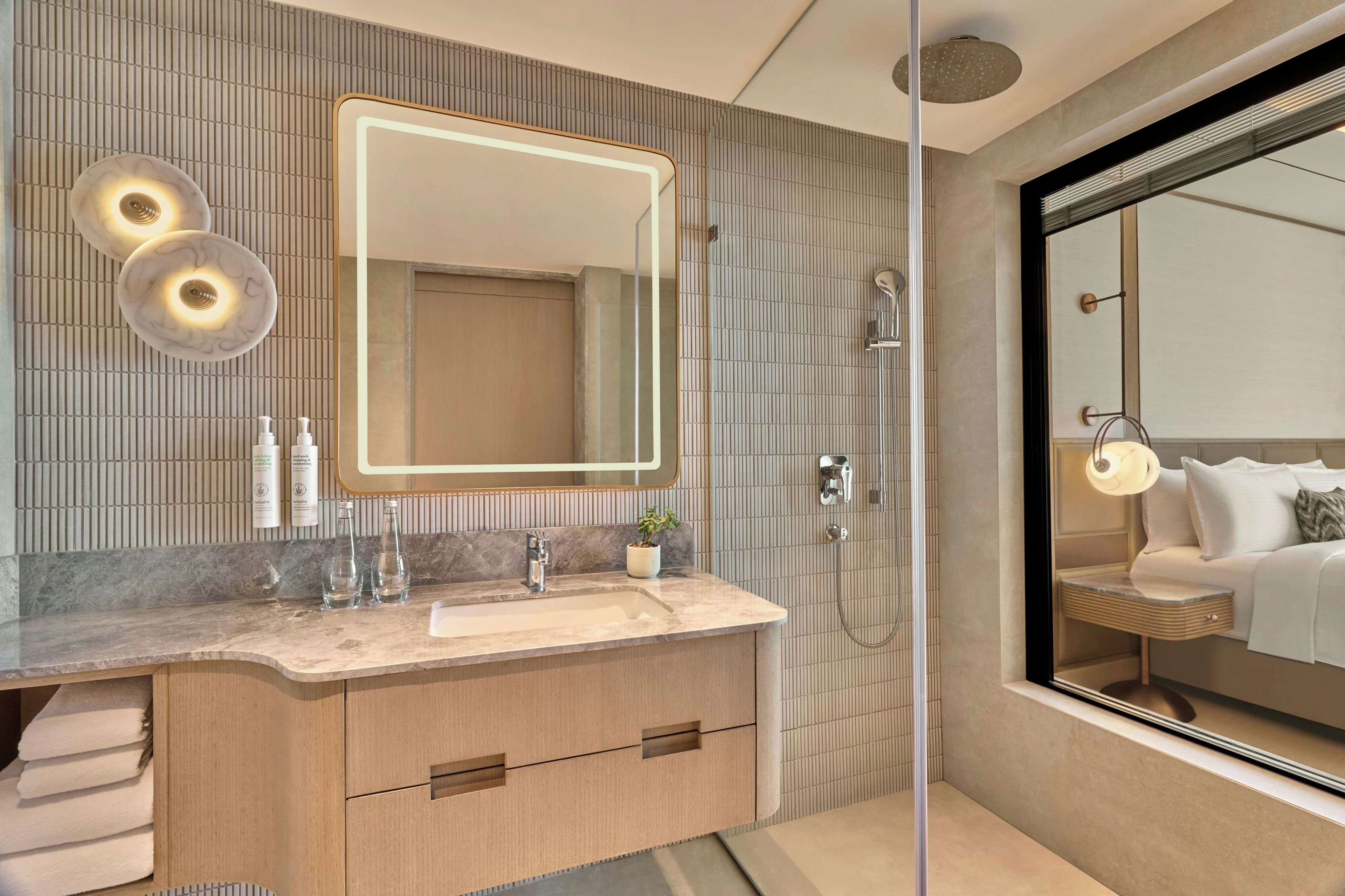 Un baño moderno con un espejo grande, un tocador con encimera de mármol y una zona de ducha.