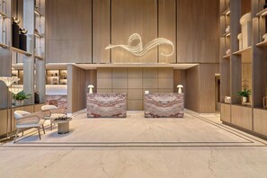 A modern lobby with marble reception desks, a central light installation, and a seating area with a round table. - Athiva Pulse Navi Mumbai, Autograph Collection (Navi Mumbai)