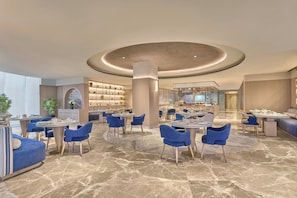 A spacious hotel lobby with multiple seating areas, a central column, and a view into the dining area.
