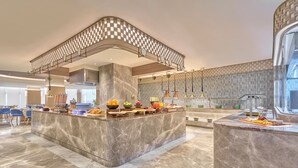 A modern kitchen with marble countertops, a central island with fruit bowls, and a patterned ceiling. - Athiva Pulse Navi Mumbai, Autograph Collection (Navi Mumbai)