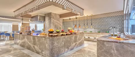 A modern kitchen with marble countertops, a central island with food, and a patterned ceiling.