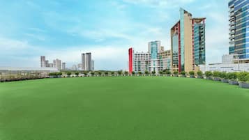 Una terraza con césped artificial, rodeada de edificios modernos con fachadas de vidrio y un cielo despejado.
