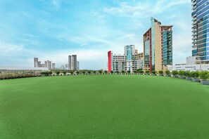 Una terraza con césped artificial, rodeada de edificios modernos con fachadas de vidrio y un cielo despejado.