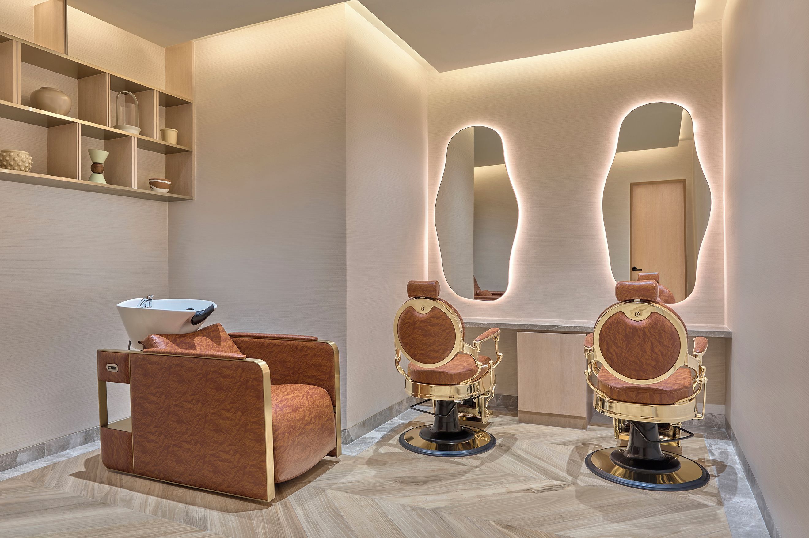 A modern bathroom with a vanity, two barber chairs, a mirror, and shelves with toiletries.